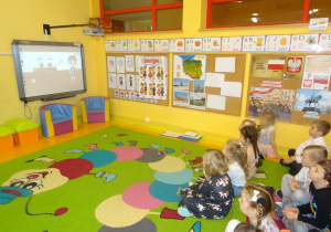 Grupa dzieci siedzi przed ekranem interaktywnym, ogląda film.